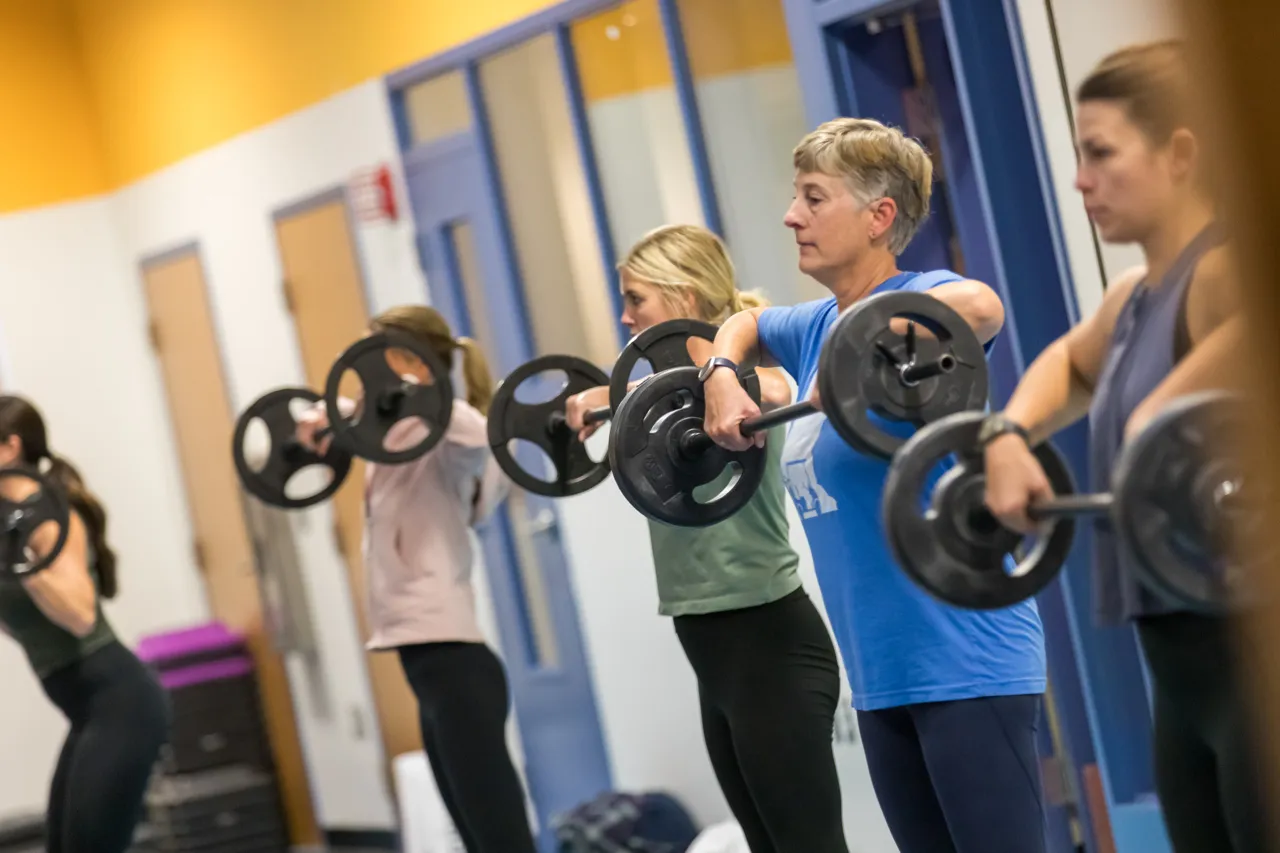 group of women lifting barbells in a fitness studio