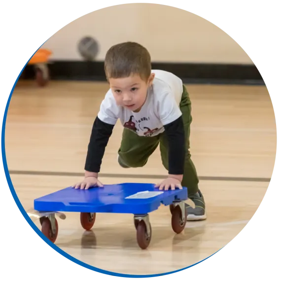 child pushing a scooter in the YMCA gymnasium