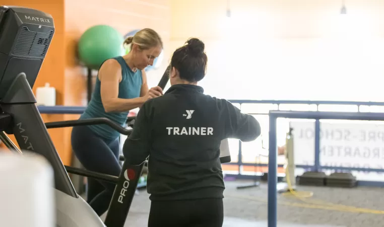 woman on an elliptical working wit ha personal trainer