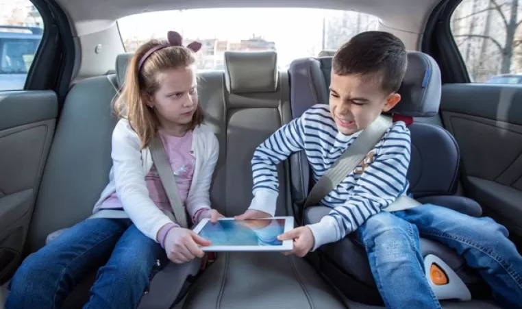young brother and sister fighting over a tablet in the back seat