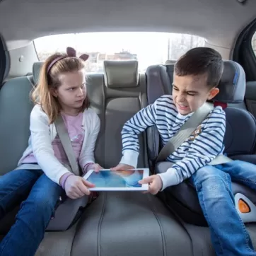 young brother and sister fighting over a tablet in the back seat